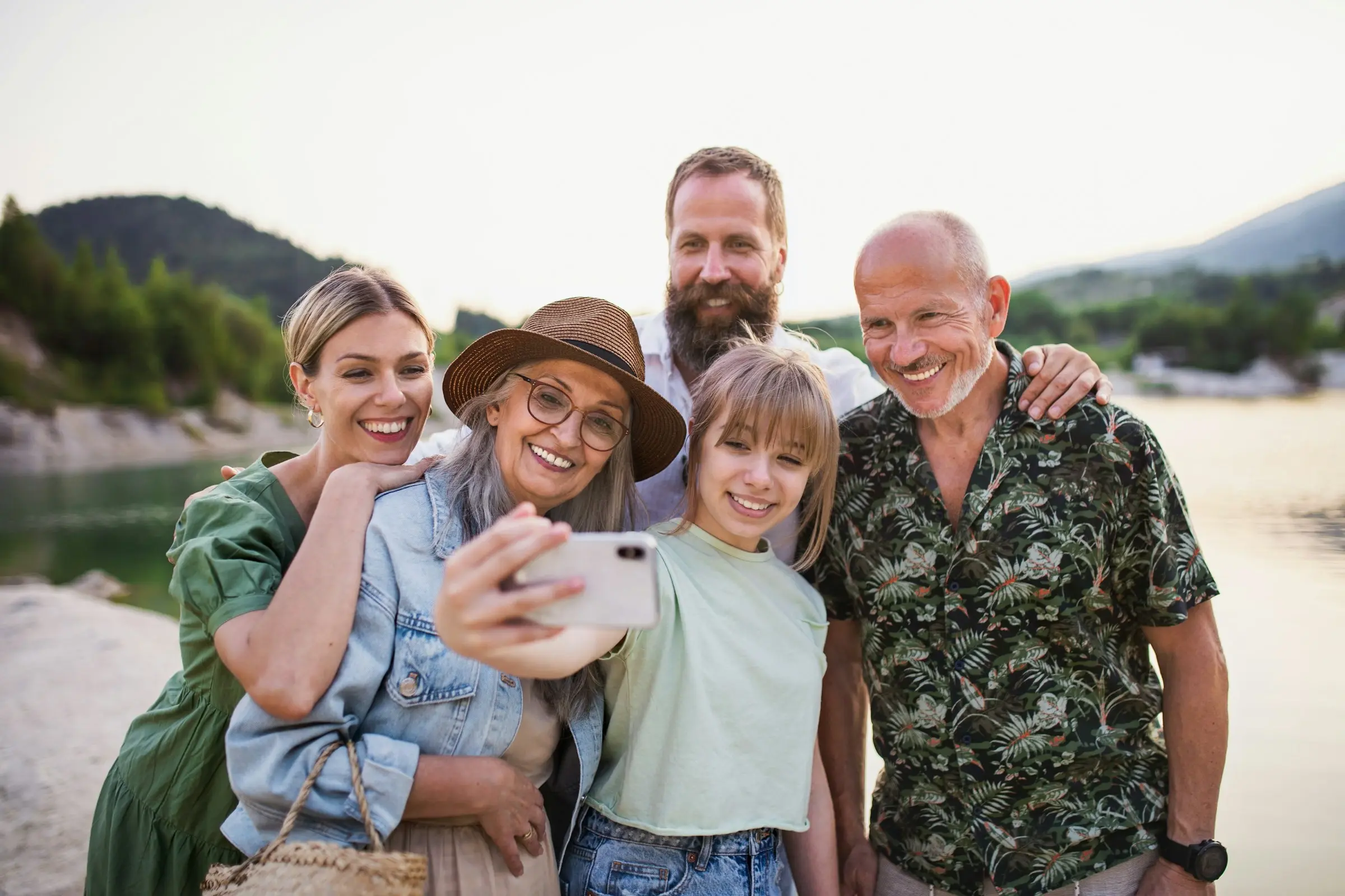 Three generations of a family taking a selfie together beside a lake at sunset