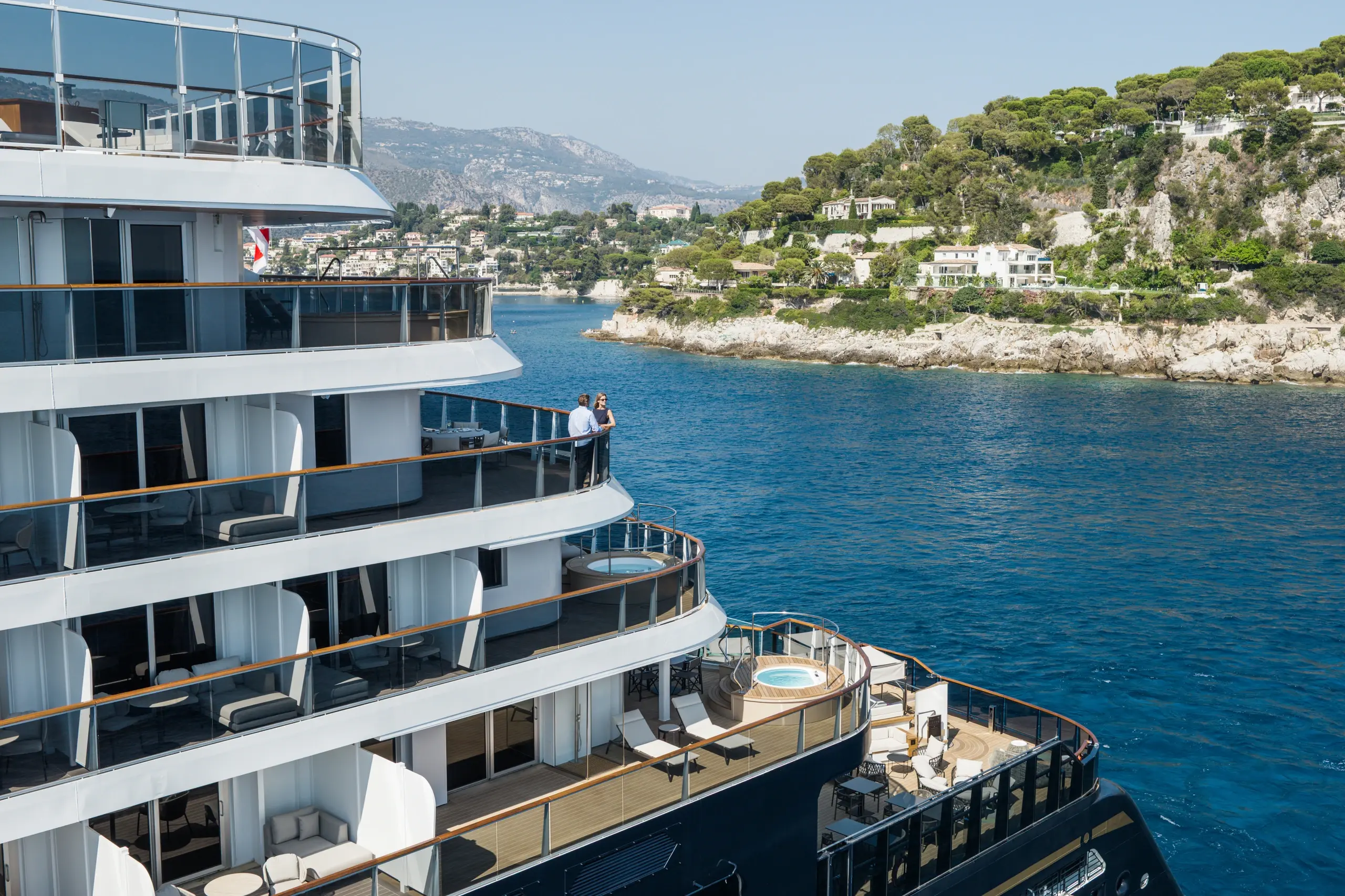 Guests on a suite terrace aboard Explora III as the ship passes a Mediterranean headland